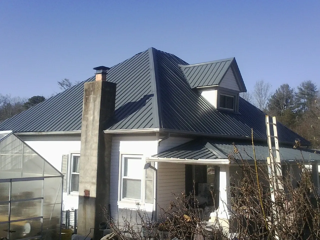Dark blue standing seam metal roof on a white farmhouse with dormer — Slate & Tile Roof Repair by Roofing Brothers in Omaha