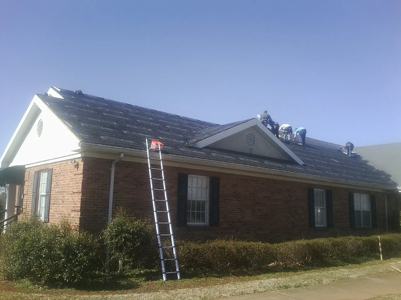 Crew tearing shingles off a brick ranch roof with a ladder set — Metal Roof Repair work by our crew in Omaha
