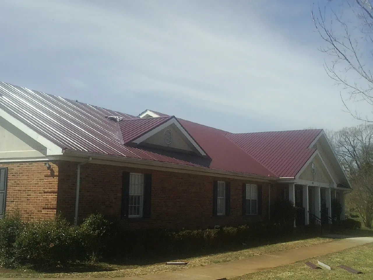 Red metal roof with gabled entries on a long brick building, from a Hail Damage Roof Repair job in Omaha