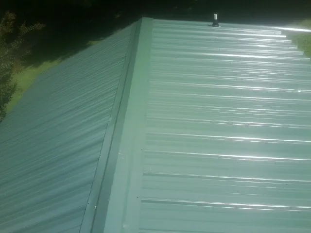 New green metal panels meeting at the ridge of a roof — Flat Roof Repair work by our crew in Omaha
