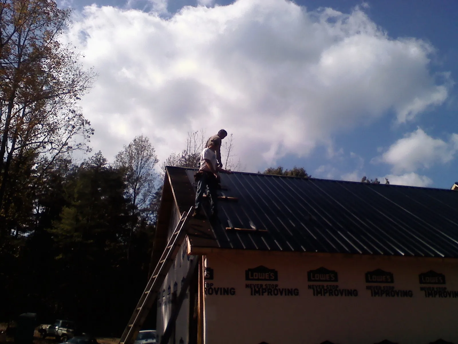 Roofer fastening dark metal panels high against a cloudy sky, from a Roof Inspection job in Omaha